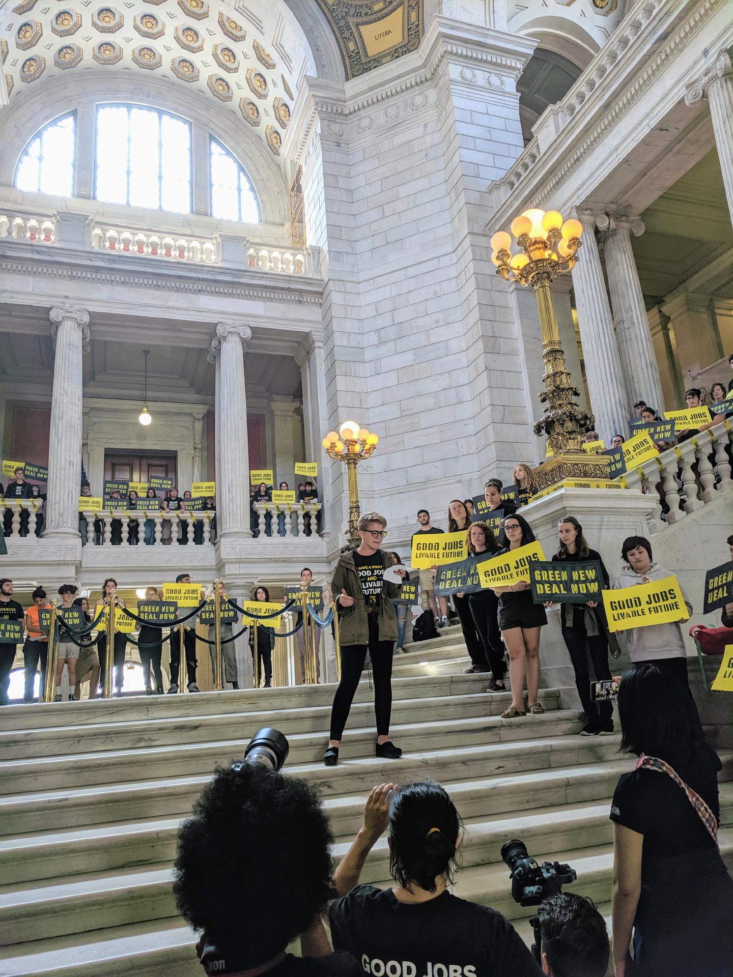 Emily addresses Sunrise Movement activists from the stairs inside the Rhode Island State House rotunda.